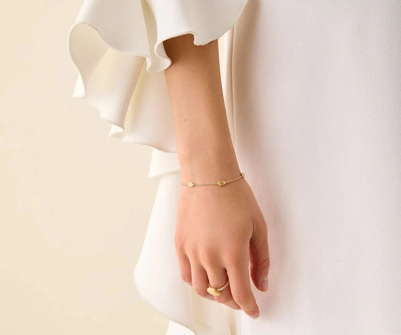 Close-up of a person's wrist wearing a gold bracelet and ring on a plain background