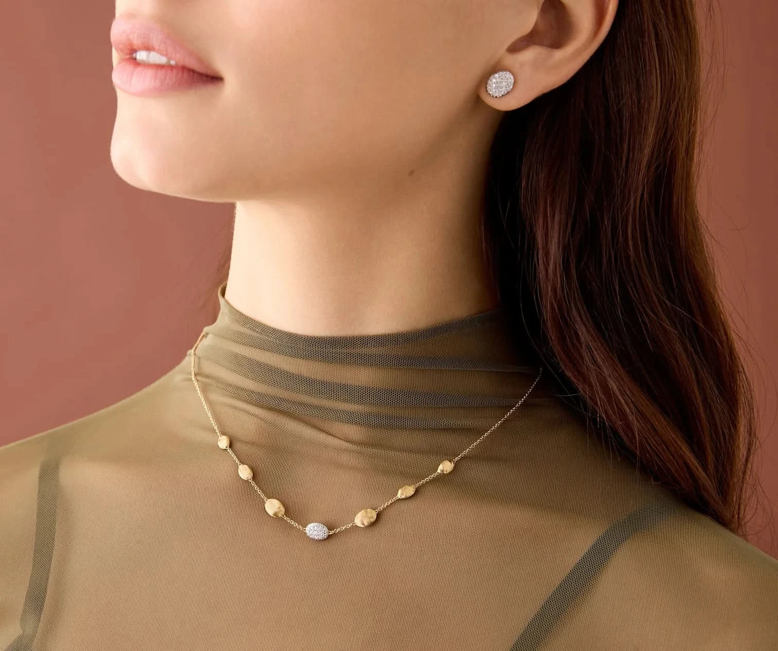 Close-up of a woman wearing gold jewelry including earrings and a necklace on a brown background