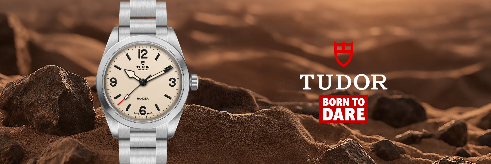 A silver Tudor watch with a cream dial is shown against a rocky desert background, with the Tudor logo and 'Born to Dare' text on the right.