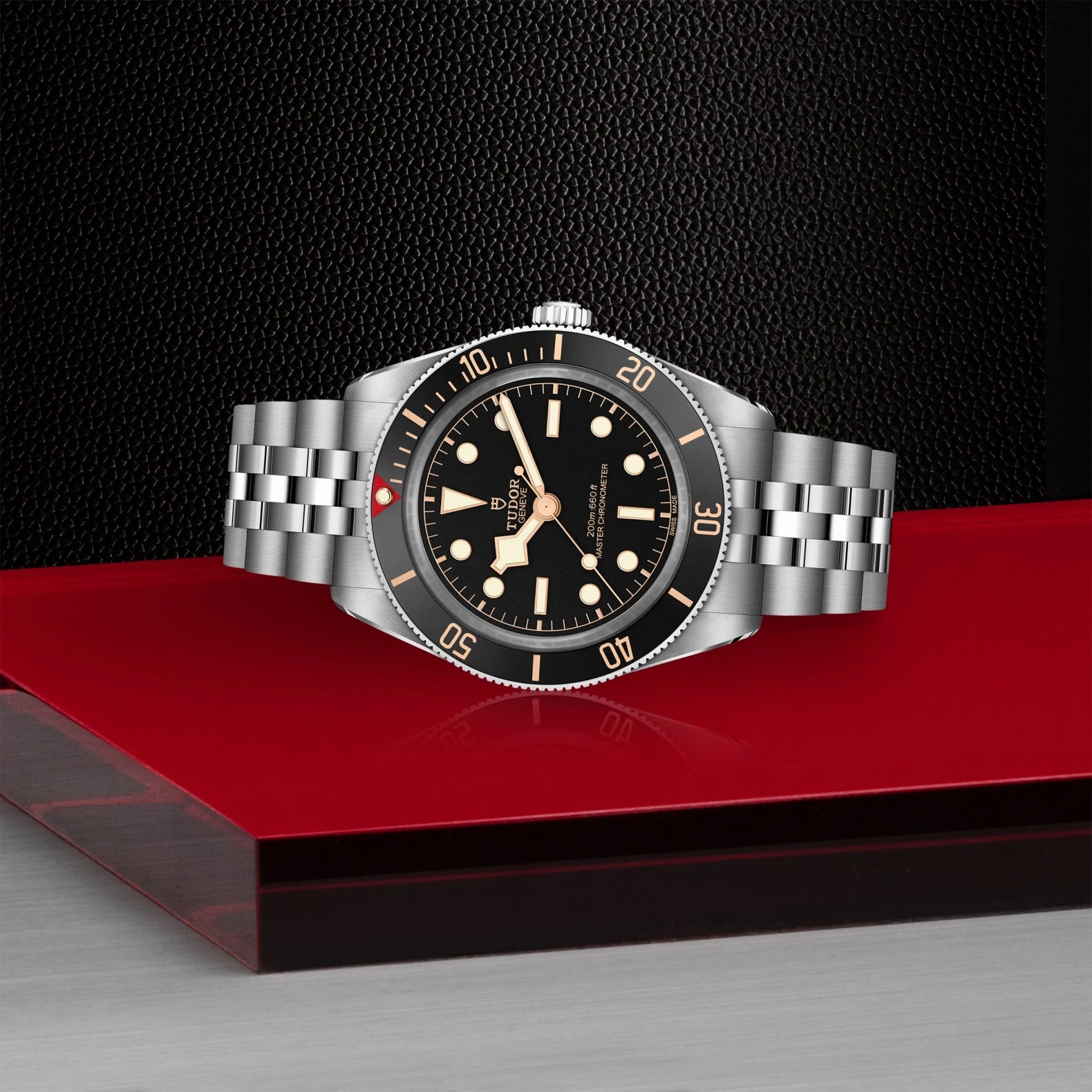 Silver watch with black dial on a red platform against a dark background