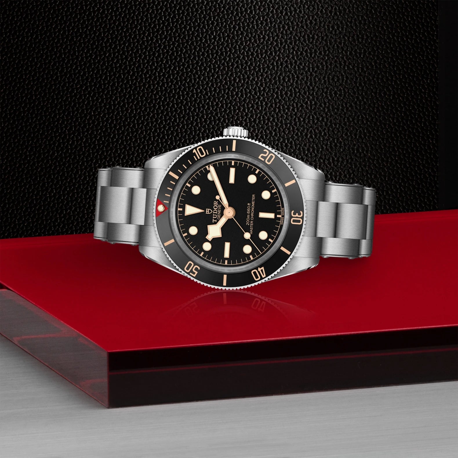 Silver watch with black dial on a red platform against a dark background