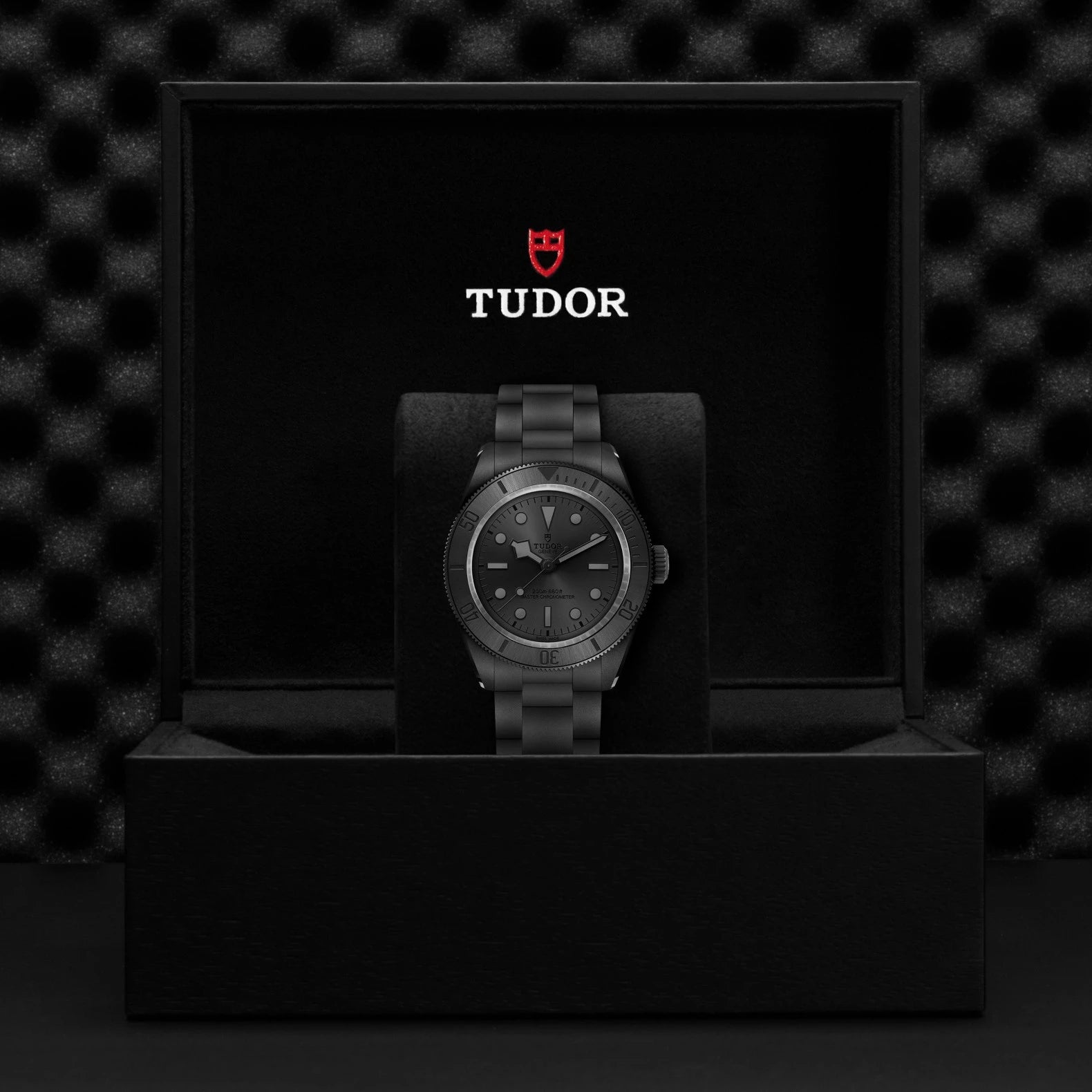 Tudor watch in a black box with the Tudor logo on a dark textured background
