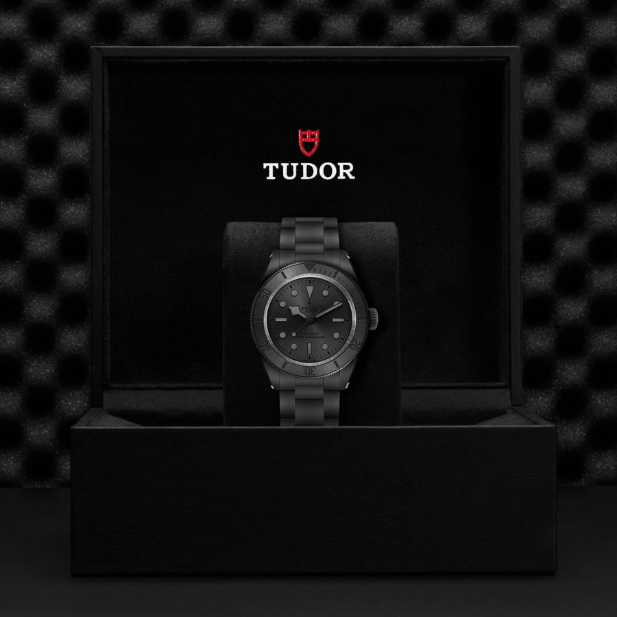 Tudor watch in a black box with the Tudor logo on a dark textured background