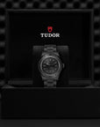 Tudor watch in a black box with the Tudor logo on a dark textured background