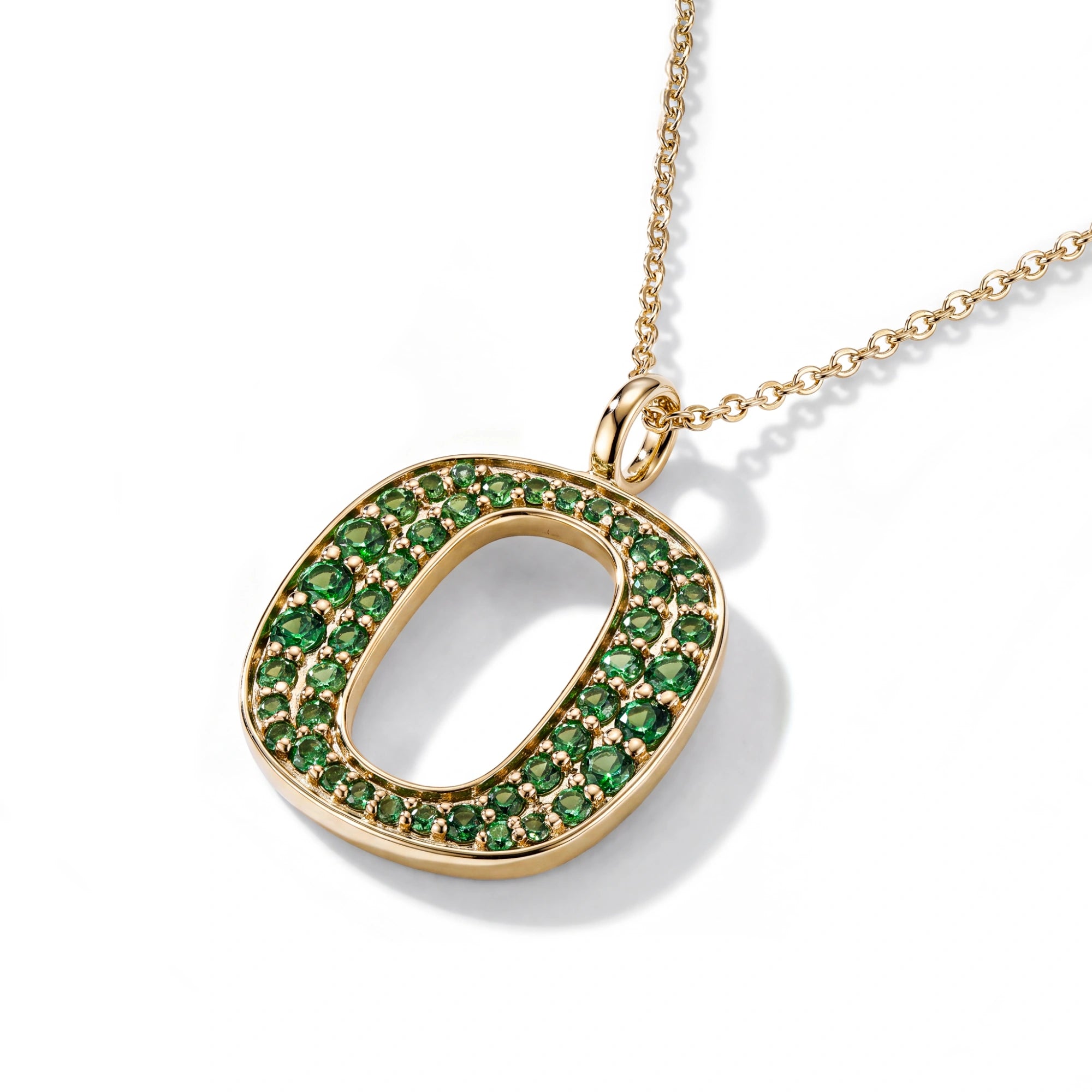 A gold initial pendant necklace featuring a large letter 'O' paved with small green gemstones, suspended from a delicate gold chain on a white background.