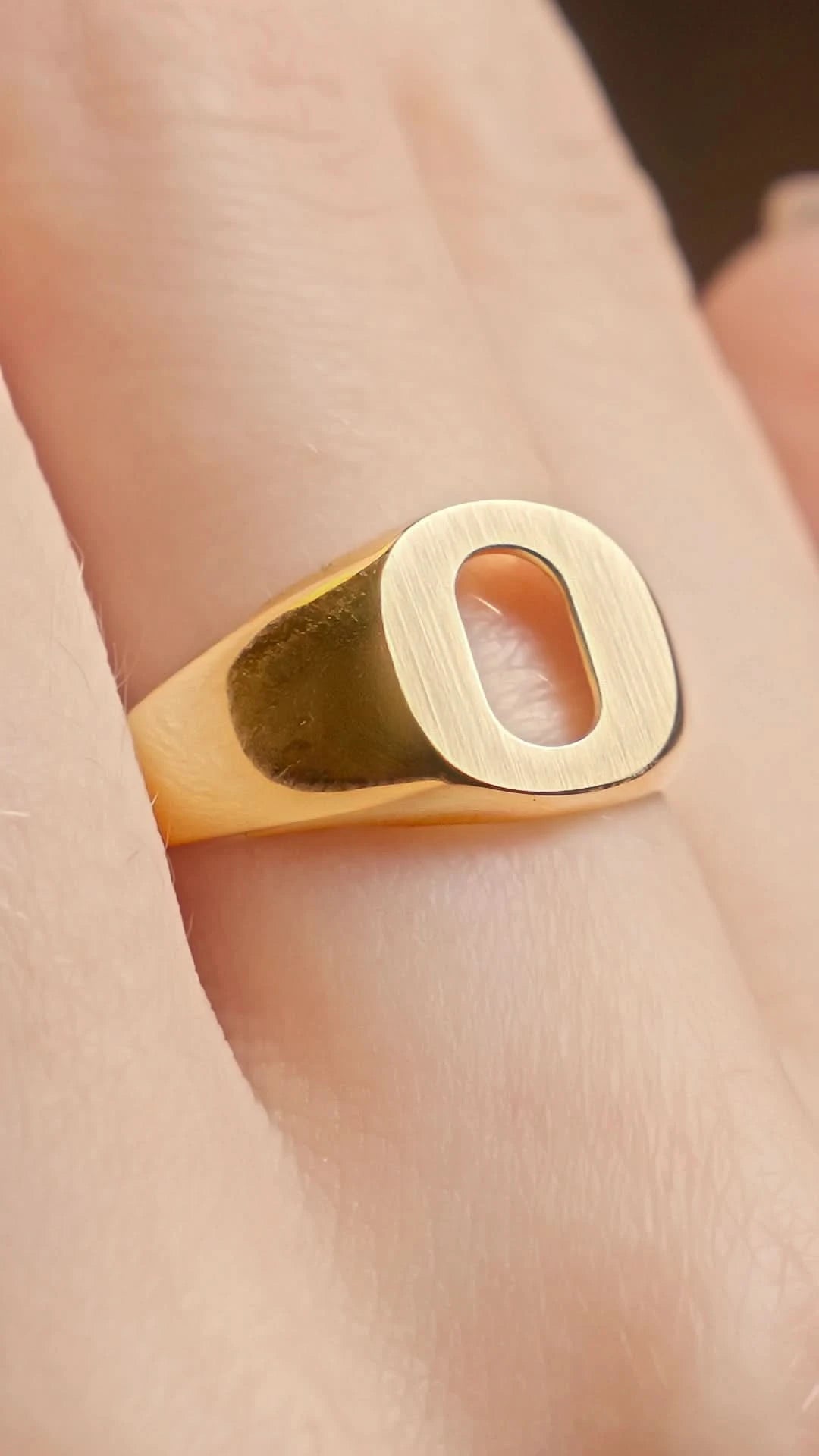 A close-up of a gold signet ring with a rectangular oval-cut face, worn on a person's finger.