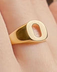A close-up of a gold signet ring with a rectangular oval-cut face, worn on a person's finger.
